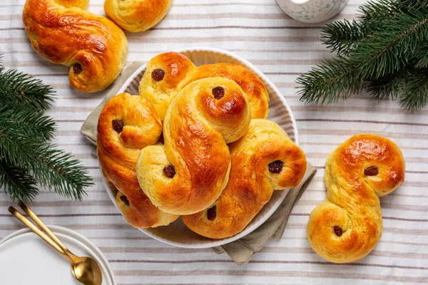 Ev yapımı, ev yapımı St Lucia safran çörekleri olan bir şölen masası. Ayrıca lussekatt ya da lussebulle, Cornish çaylı çöreği ya da mercimek ekmeği, safranlı tatlı çörek ve kuru üzüm içerir. Beyaz bir masa örtüsünün üzerinde