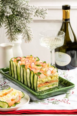 Swedish sandwich cake Smorgastarta on a Christmas eve  table, white wine. Layers of bread bound with filling egg and mayonnaise, salmon fish, avocado, prawns, decorated with cucumbers and radish. clipart