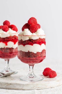 Red Velvet Trifle, kırmızı kadife pasta katmanları, peynirli mascarpone kremi, böğürtlen reçeli, taze ahududu, bardakta servis edilir. Noel ya da Sevgililer Günü için ev yapımı bir tatlı. Dikey resim.