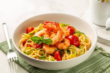 Beyaz tabakta İtalyan deniz ürünleri ve sebze makarnası. Karides, domates ve kabak ya da kabak, spagetti..