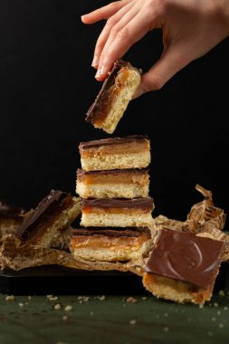 Kızlar ellerinde karamel dilimleri, dilimler ya da milyonerlerin kurabiyeleri olarak da bilinen bir parça karamelli kurabiye tutuyorlar. Tatlı, karamelli ve çikolatalı kurabiye tabanlı kek. Dikey resim.