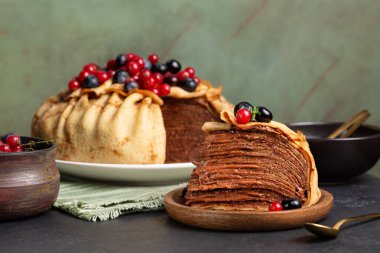 Ev yapımı krep, ince krep ve çikolata kremasından yapılmış, yaban mersini ve kırmızı üzümle süslenmiş. Koyu yeşil arkaplan.