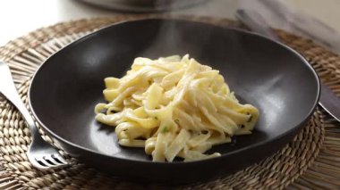 Siyah tabakta kremalı fettuccine Alfredo makarnası servis ediyorum.