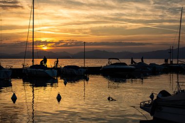 2024-04-28 Lazise, İtalya. Küçük İtalyan kasabası dışında, Garda Gölü 'nde teknelerin silueti olan bir liman manzarası. Akşam vakti, altın saat..