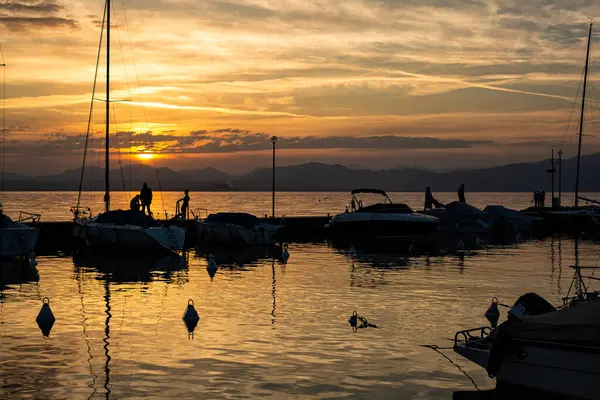 2024-04-28 Lazise, İtalya. Küçük İtalyan kasabası dışında, Garda Gölü 'nde teknelerin silueti olan bir liman manzarası. Akşam vakti, altın saat..