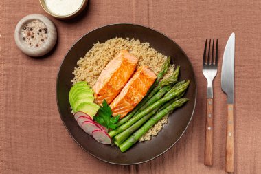 Somon, kinoa ve kuşkonmazlı tabağın üst görüntüsü, moka renkli tekstil arka planında redish ve avokado.