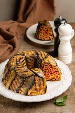 Patlıcan Timballo di Melanzane. Makarna ve domatesin etrafına kızarmış patlıcan, peynir ve fırın. İtalyan yemeği. Kahverengi masa yüzeyi. Dikey resim.