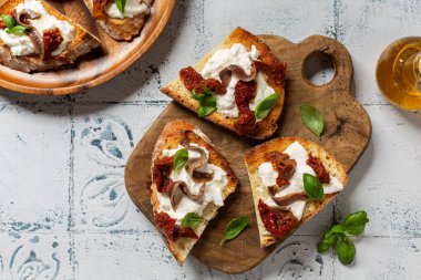 Kurutulmuş domates, ançüez, fesleğen ve burrata peynirli crostini. Üst Manzara. Beyaz tyle tablo yüzeyi.