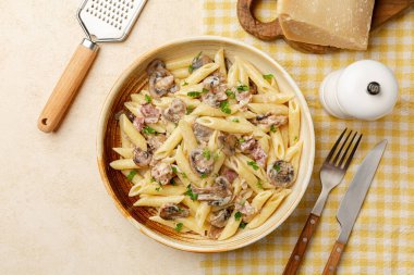 Top view of creamy pasta penne with mushrooms and bacon. Hard cheese and grater. Copy space, beige table surface.