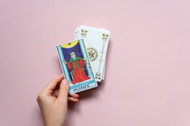 London, UK: 14 October, 2022: The 11 Major Arcana - Justice Tarot Card of Rider Waite deck in hand on pink background clipart