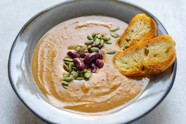 Healthy vegan pumpkin soup with red beans, pumpkin seeds, coconut cream and slices of fried bread