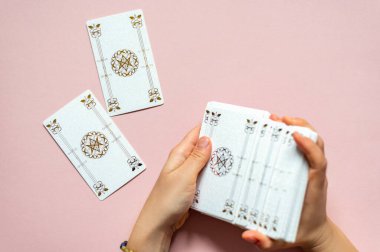 Falcı kadının elleri ve beyaz tarot kartları. Rider Waite destesinin klasik kart yığını pembe arka planda