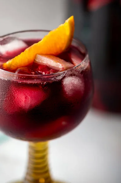 Glass of traditional red sangria with red wine, ice and fruits, light background
