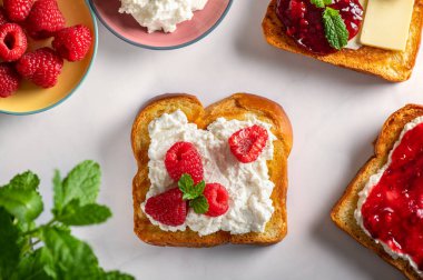 Brioche ekmeği dilimleri, ricotta peyniri, tereyağı, taze ahududu ve ahududu reçeli ve nane yapraklı açık sandviçli lezzetli kahvaltı.