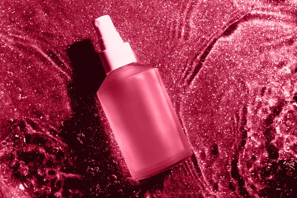 Mat glass bottle of body oil on viva magenta color water background, glass cosmetics in water , top view. Color of the year 2023