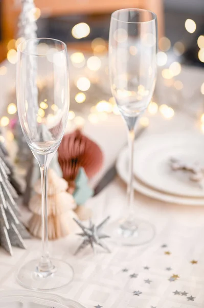 背景にトレンディーな紙のクリスマスツリーと白とピンクの色のクリスマステーブル設定 空のプレートとお祝いのディナーやパーティーの準備ができてメガネ — ストック写真