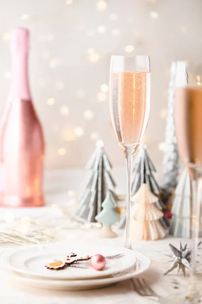 背景にトレンディーな紙のクリスマスツリーと白とピンクの色のクリスマステーブルの設定 テーブルの準備ができているお祝いの夕食とパーティーピンクの検察官がガラスに注ぐ — ストック写真