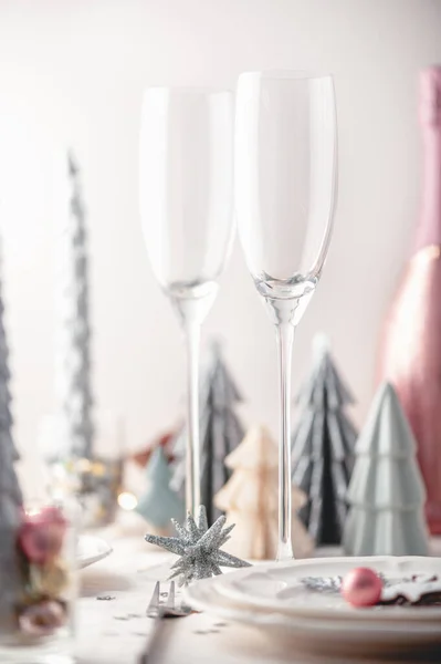 背景にトレンディーな紙のクリスマスツリーと白とピンクの色のクリスマステーブル設定 空のプレートとお祝いのディナーやパーティーの準備ができてメガネ — ストック写真