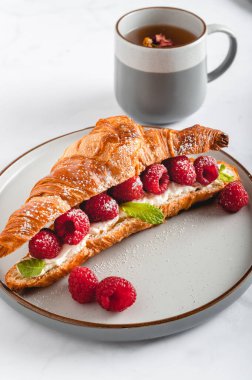 Kahvaltıda kruvasan, ricotta veya krem peynirli, taze ahududu ve nane yapraklı lezzetli sandviçler.