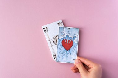 London, UK: 6 January, 2023: Minor Arcana - Three of Swords of Tarot Card of Rider Waite deck in hand on pink background clipart