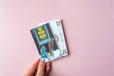 London, UK: 6 January, 2023: Minor Arcana - Five of Pentacles of Tarot Card of Rider Waite deck in hand on pink background