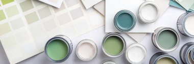 Tiny sample paint cans during house renovation, process of choosing paint for the walls, different green and beige colors, color charts on background