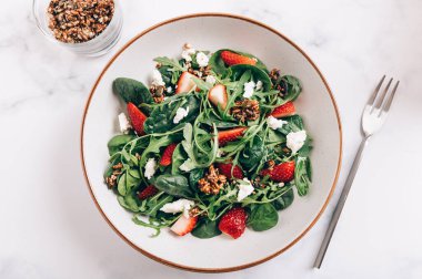Yeşil Salata Yaprakları, Roket Salatası, Taze Çilek Dilimleri, Feta Peyniri ve Farklı Tohumlardan yapılmış sağlıklı salata.