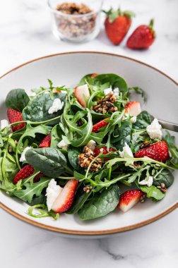 Yeşil Salata Yaprakları, Roket Salatası, Taze Çilek Dilimleri, Feta Peyniri ve Farklı Tohumlardan yapılmış sağlıklı salata.