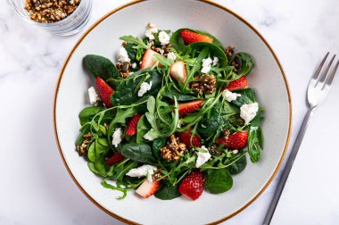 Yeşil Salata Yaprakları, Roket Salatası, Taze Çilek Dilimleri, Feta Peyniri ve Farklı Tohumlardan yapılmış sağlıklı salata.