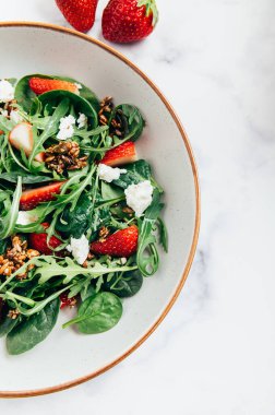 Yeşil Salata Yaprakları, Roket Salatası, Taze Çilek Dilimleri, Feta Peyniri ve Farklı Tohumlardan yapılmış sağlıklı salata.