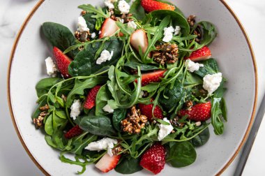 Yeşil Salata Yaprakları, Roket Salatası, Taze Çilek Dilimleri, Feta Peyniri ve Farklı Tohumlardan yapılmış sağlıklı salata.