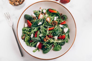 Yeşil Salata Yaprakları, Roket Salatası, Taze Çilek Dilimleri, Feta Peyniri ve Farklı Tohumlardan yapılmış sağlıklı salata.