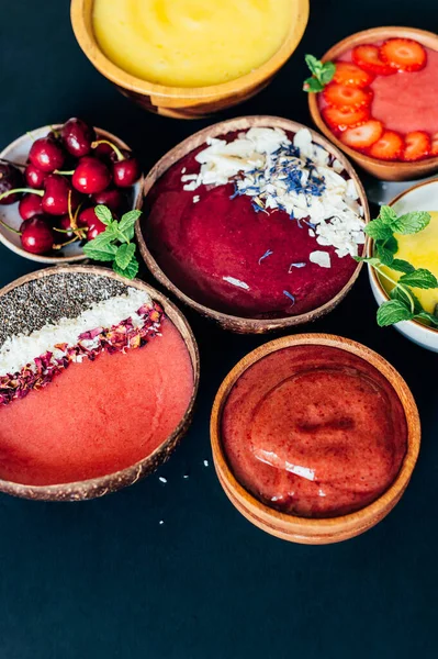 stock image Variety of different smoothies: Banana and Strawberries, Cherry and Apple, Pineapple and Mango with pieces of Strawberries, Coconut Shreds, Chia Seeds and rose petals on top in the Coconut Shell Bowl