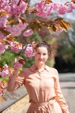 30 'lu yaşlarının ortalarında parkta çiçek açan kiraz ağacı ya da Sakura' lı bir kadın. İngiltere 'de ilkbahar. Hayatın ve güneşli havanın tadını çıkarıyorum.