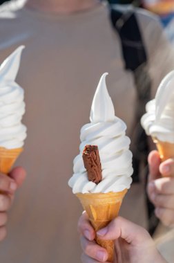 Soft whipped vanilla ice cream with chocolate stick in waffle cone in hands