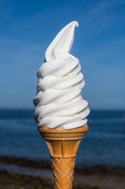 Yumuşak çırpılmış vanilyalı dondurma ve çikolatalı waffle külahı. Mavi gökyüzü arka planında.