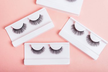 Moda pastel pembe arka planda kutularda farklı sahte kirpikler. Makyaj malzemeleri. Kadınlar için kozmetik ürünleri. Üst manzara, düz yatış. Yerleşim planı. Metin ve tasarım için yer.