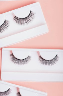 Moda pastel pembe arka planda kutularda farklı sahte kirpikler. Kadınlar için makyaj malzemeleri ve güzellik kozmetik ürünleri. Üst manzara, düz uzanma.