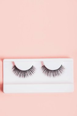 Moda pastel pembe arka planda kutularda farklı sahte kirpikler. Makyaj malzemeleri. Kadınlar için kozmetik ürünleri. Üst manzara, düz yatış. Yerleşim planı. Metin ve tasarım için yer.