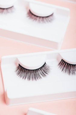 Moda pastel pembe arka planda kutularda farklı sahte kirpikler. Kadınlar için makyaj malzemeleri ve güzellik kozmetik ürünleri. Üst manzara, düz uzanma.