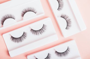 Moda pastel pembe arka planda kutularda farklı sahte kirpikler. Kadınlar için makyaj malzemeleri ve güzellik kozmetik ürünleri. Üst manzara, düz uzanma.