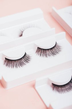 Moda pastel pembe arka planda kutularda farklı sahte kirpikler. Kadınlar için makyaj malzemeleri ve güzellik kozmetik ürünleri. Üst manzara, düz uzanma.
