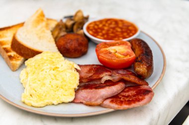 Sosis, mantar, domates, pastırma, ev yapımı haşlanmış et, fasulye, çırpılmış yumurta ve tereyağlı ekmek ile tam İngiliz kahvaltısı.