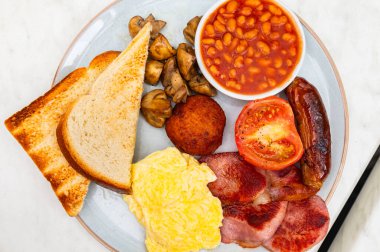 Sosis, mantar, domates, pastırma, ev yapımı haşlanmış et, fasulye, çırpılmış yumurta ve tereyağlı ekmek ile tam İngiliz kahvaltısı.