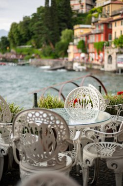 Güneşli bir yaz öğleden sonrasında, Varenna rıhtımında boş sandalyeli güzel bir kafe rüzgarlı bulutlu bir günde, Como Gölü, Lombardy, İtalya
