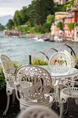 Güneşli bir yaz öğleden sonrasında, Varenna rıhtımında boş sandalyeli güzel bir kafe rüzgarlı bulutlu bir günde, Como Gölü, Lombardy, İtalya