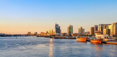 Gökdelenleri, geleneksel tekneleri ve rıhtımları olan Dubai Deresi 'nin Skyline manzarası. Güneşli yaz gününde gün batımı. Dubai, BAE 'deki en ünlü turizm merkezidir. Dubai 'de modern ve eski yaşam tarzının karışımı.