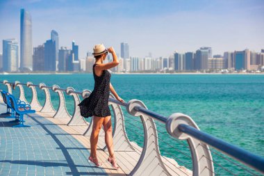 Turist kadın deniz ve gökdelenlerle Abu Dabi manzarasının keyfini çıkarıyor. Abu Dabi 'de güneşli bir yaz günü. BAE' nin ünlü turistik beldesi. Lüks seyahat ve dinlenme için ideal bir yer.