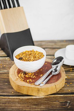 Kahvaltının düzeninde paslanmaz çelik kaşıklar ve arka planda bulanık mutfak bıçağı tutacağı olan tahtadan tahıllı beyaz kase.