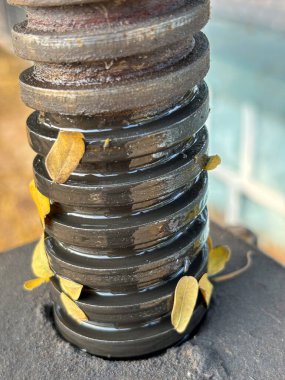 Üzerinde sarı yapraklar saçılmış siyah metal bir yay, endüstriyel ve doğal elementlerin bir karışımını sergiliyor..